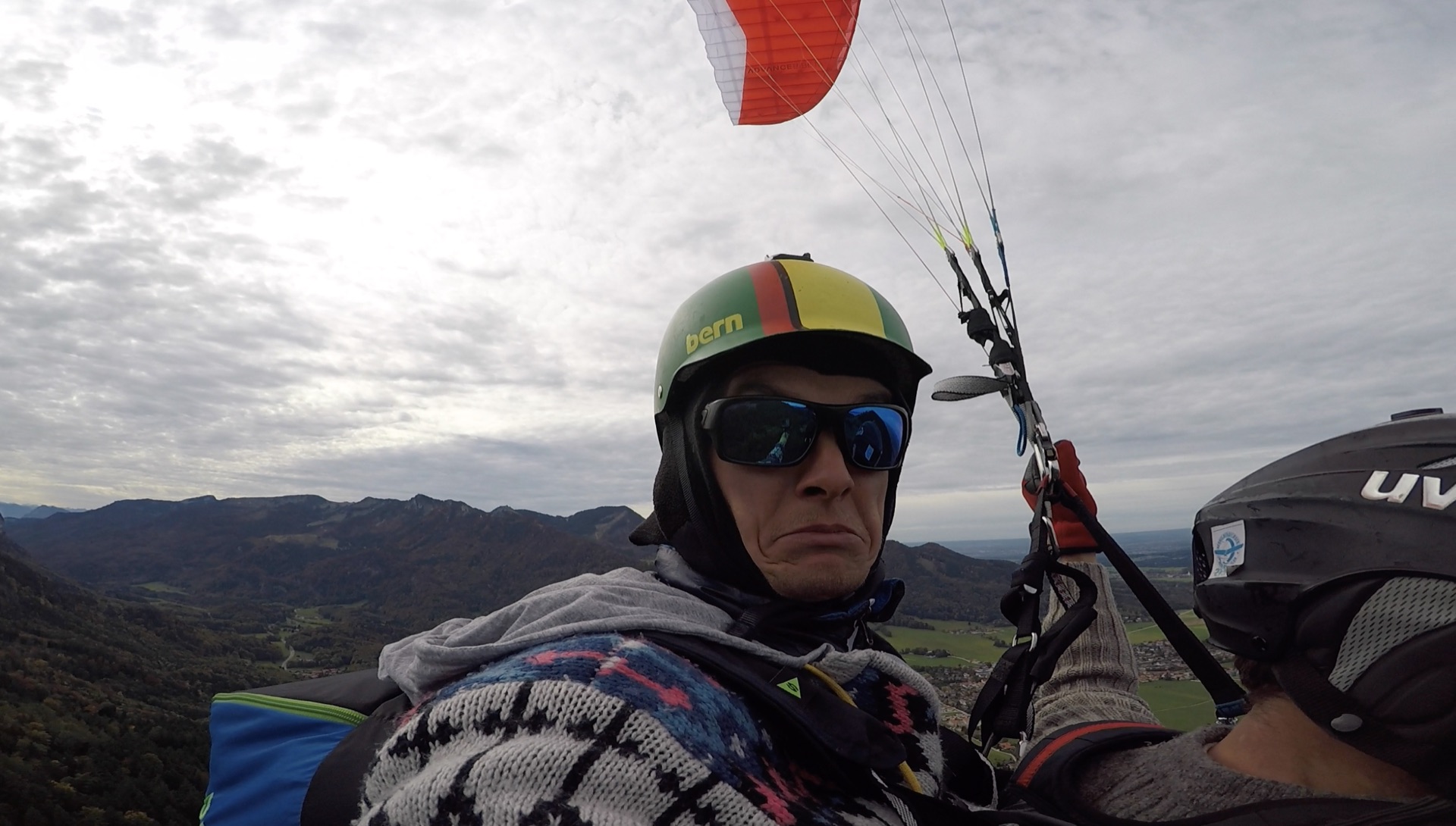 Simon Schnittker als Pilot mit Gleitschirm und Bergen im Hintergrund